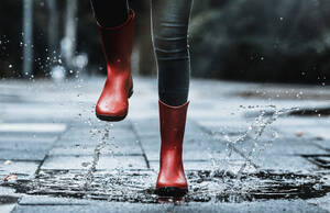Mädchen in Gummistiefeln spritzt beim Springen in eine Pfütze auf dem Fußweg mit Wasser - FLLF00507
