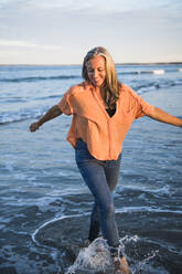 Grauhaarige Frau spielt am Strand zum Sonnenuntergang - CAVF90632