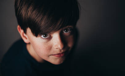 Close up portrait of young brunette boy with freckles in dark room. - CAVF90660