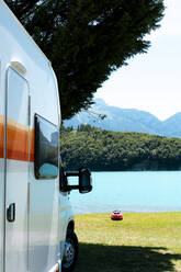 RV Wohnmobil vor einem blauen See mit Bergen und einem roten Kajak - CAVF90724
