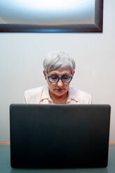 Kaukasische ältere Frau mit weißen Haaren und blauer Brille mit einem Laptop - CAVF90727