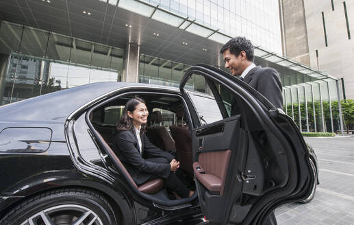 Chauffeur öffnet Autotür für Geschäftsfrau in Bürogebäude - CAVF90755