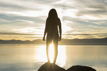 Rückansicht der Silhouette einer Frau auf einem Felsen am Lake Tahoe bei Sonnenuntergang - CAVF90768