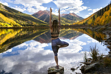 Rear view of woman practicing yoga on rock by lake - CAVF90784