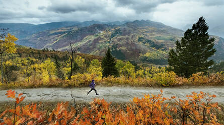 Woman running on road during autumn - CAVF90786