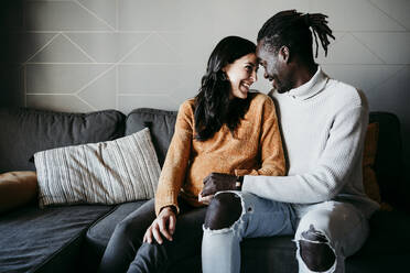 Romantischer Mann und schwangere Frau sehen sich gegenseitig an, während sie zu Hause auf dem Sofa sitzen - EBBF01625