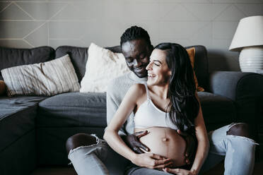 Glückliche schwangere Frau und junger Mann verbringen ihre Freizeit zusammen zu Hause - EBBF01628