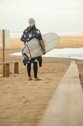 Männlicher Surfer mit Surfbrett auf der Promenade am Strand - KBF00621