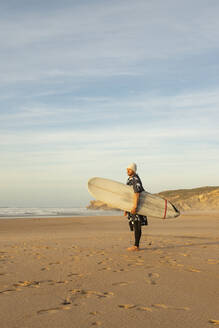 Mittlerer erwachsener männlicher Surfer mit Surfbrett am Strand gegen den Himmel - KBF00623