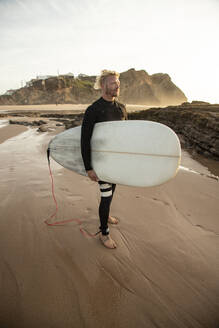 Blonder männlicher Surfer mit Surfbrett am Strand gegen den Himmel - KBF00631