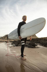 Männlicher Surfer mit Surfbrett am Strand gegen den Himmel - KBF00632