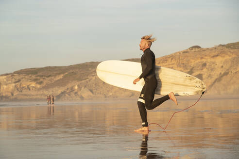Mann läuft mit Surfbrett am Strand bei Sonnenuntergang - KBF00638