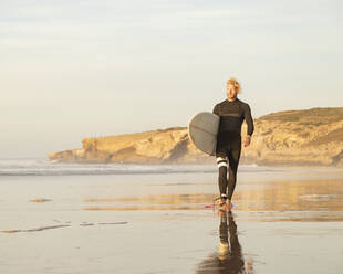 Männlicher Surfer mit Surfbrett läuft am Strand gegen den Himmel - KBF00639