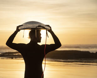 Silhouette Surfer trägt Surfbrett über Kopf am Strand bei Sonnenuntergang - KBF00644