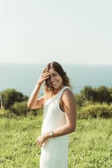 Lächelnde junge Frau steht im Park gegen den Himmel an einem sonnigen Tag - MTBF00700