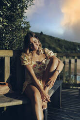 Lächelnde Frau sitzt auf einer Bank im Park bei Sonnenuntergang - MTBF00706