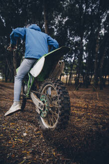 Jugendlicher, der einen Motorradreifen dreht, während er im Wald Schmutz aufwirbelt - ACPF00903
