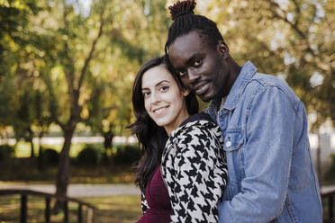 Smiling multi ethnic couple embracing while standing in park - EBBF01653