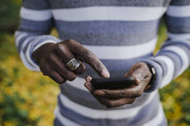 Man holding smart phone in park during autumn - EBBF01687