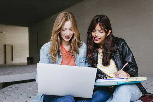 Junge Studentin, die einen Laptop benutzt, während sie gemeinsam auf dem Universitätscampus studiert - TCEF01350