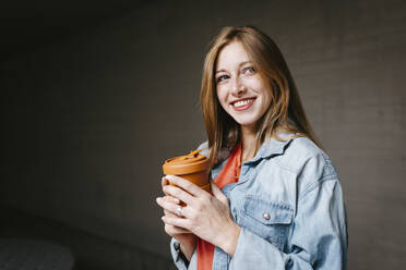 Glückliche schöne junge Frau mit wiederverwendbarem Kaffeebecher auf dem Universitätscampus - TCEF01353