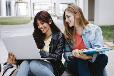 Junge Studentinnen lächelnd bei der Benutzung eines Laptops auf dem Campus - TCEF01358