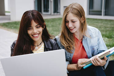 Lächelnde junge multiethnische Studentin bei der Benutzung eines Laptops auf dem Campus - TCEF01359