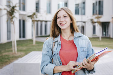 Happy young female Caucasian student looking away at university campus - TCEF01373