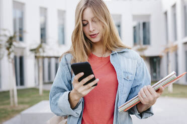 Junge blonde Studentin mit Smartphone an der Universität - TCEF01374