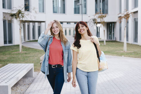 Fröhliche junge multiethnische Studentinnen, die über den Universitätscampus spazieren - TCEF01376