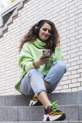 Young woman enjoying music while using mobile phone on steps - PNAF00246