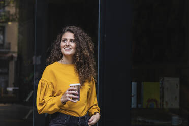 Lächelnde Frau mit lockigem Haar, die eine Kaffeetasse hält und wegschaut - PNAF00263