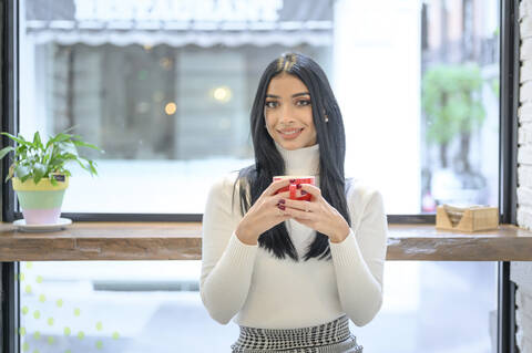 Smiling businesswoman holding cup of coffee against window in cafe stock photo