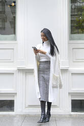 Lächelnde Geschäftsfrau mit Mobiltelefon vor weißer Wand - PGF00246
