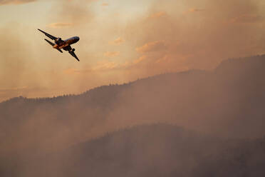 Militärflugzeug fliegt bei Sonnenuntergang über den Rauch eines Waldbrandes - CAVF90810