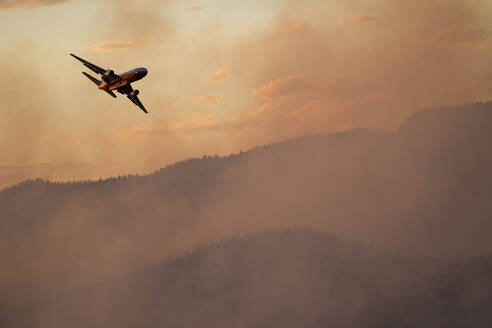 Militärflugzeug fliegt bei Sonnenuntergang über den Rauch eines Waldbrandes - CAVF90810