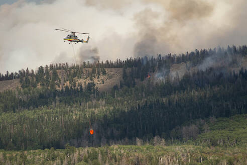 Militärhubschrauber fliegt mit Brandbekämpfungsmitteln, während Rauch aus dem Wald aufsteigt - CAVF90817