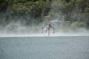 Militärhubschrauber fliegt über den See, während im Hintergrund Rauch von einem Waldbrand aufsteigt - CAVF90824