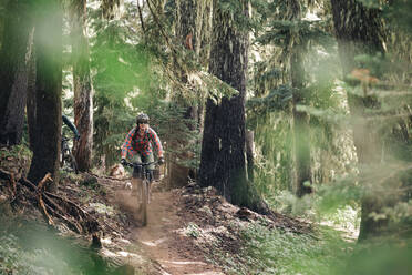 A young woman rides her ike through the forest at Mt. Hood, Oregon. - CAVF90840