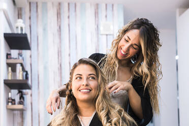 Hairdresser combing client with long curly hair against wall mirror at Hair Salon - CAVF90885