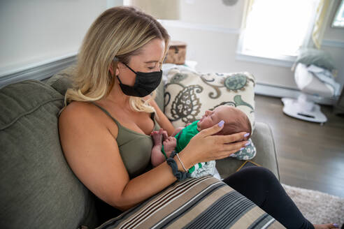 Blonde Frau mit Gesichtsmaske hält ein schläfriges Neugeborenes. - CAVF90892