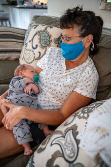 Frau mit Gesichtsmaske hält ihren Enkel. - CAVF90893