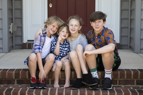 Vier Geschwister sitzen zusammen auf einer Backsteintreppe in nicht zusammenpassenden Outfits - CAVF90904