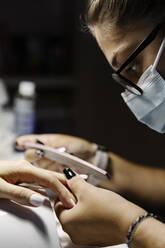 Woman in mask shaping nails of client while working during epidemic - CAVF90908