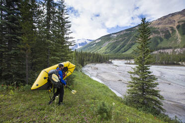 Explorer carries inflatable boat down to river in Banff National Park. - CAVF90922