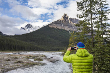 Man in green jacket takes a photo of Alexandra Mountain, Banff, Canada - CAVF90926