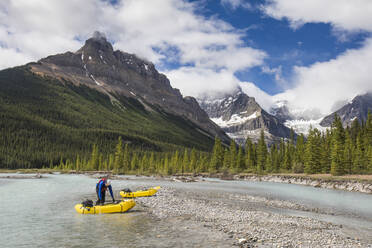 Paddler prepares to launch yellow inflatable raft into scenic river. - CAVF90930
