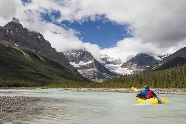 Explorer paddles yellow raft towards the Rocky Mountains, Banff. - CAVF90931