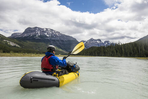 Ein Mann paddelt auf einem gelben Floß durch ein weites Tal im Banff National Park. - CAVF90933