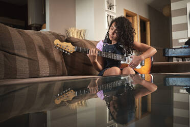 Ein kleines Mädchen, das sich beim Gitarrenspiel im Wohnzimmer konzentriert - CAVF90949